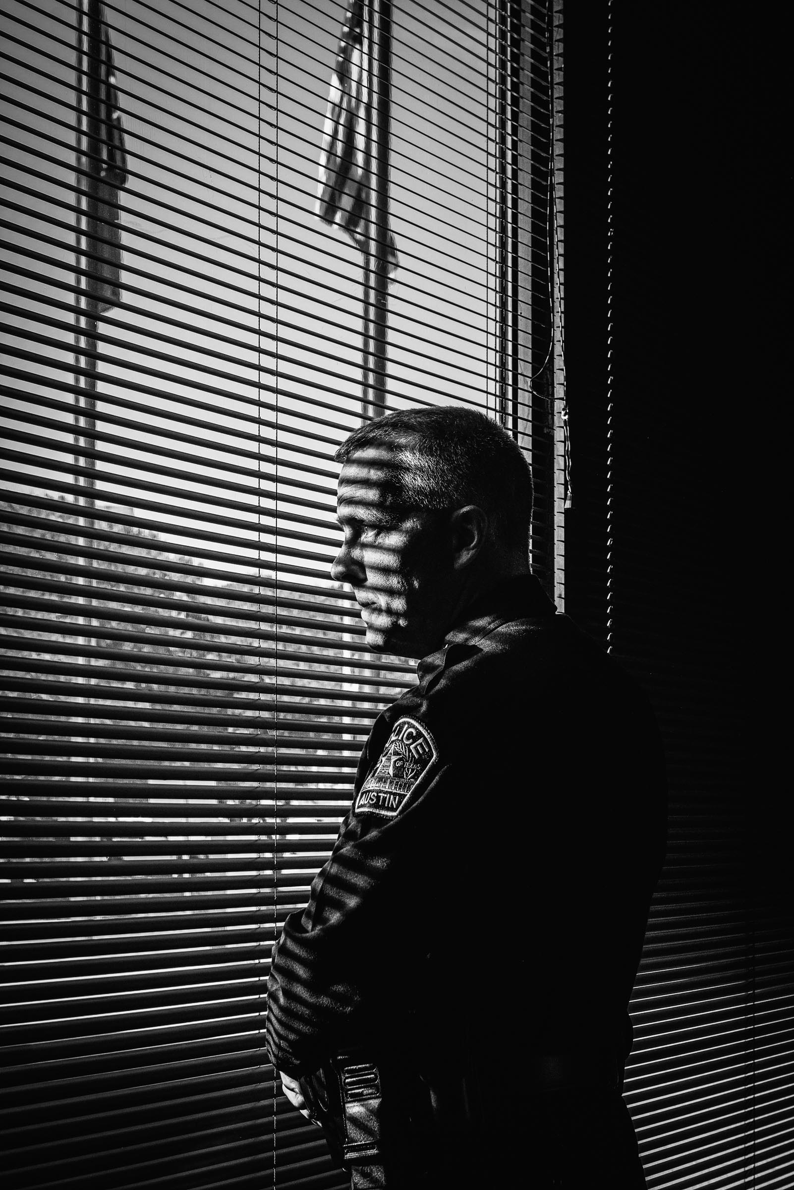 Black-and-white portrait of pensive Austin-Police-Chief-Brian-Manley- peering through blinds.