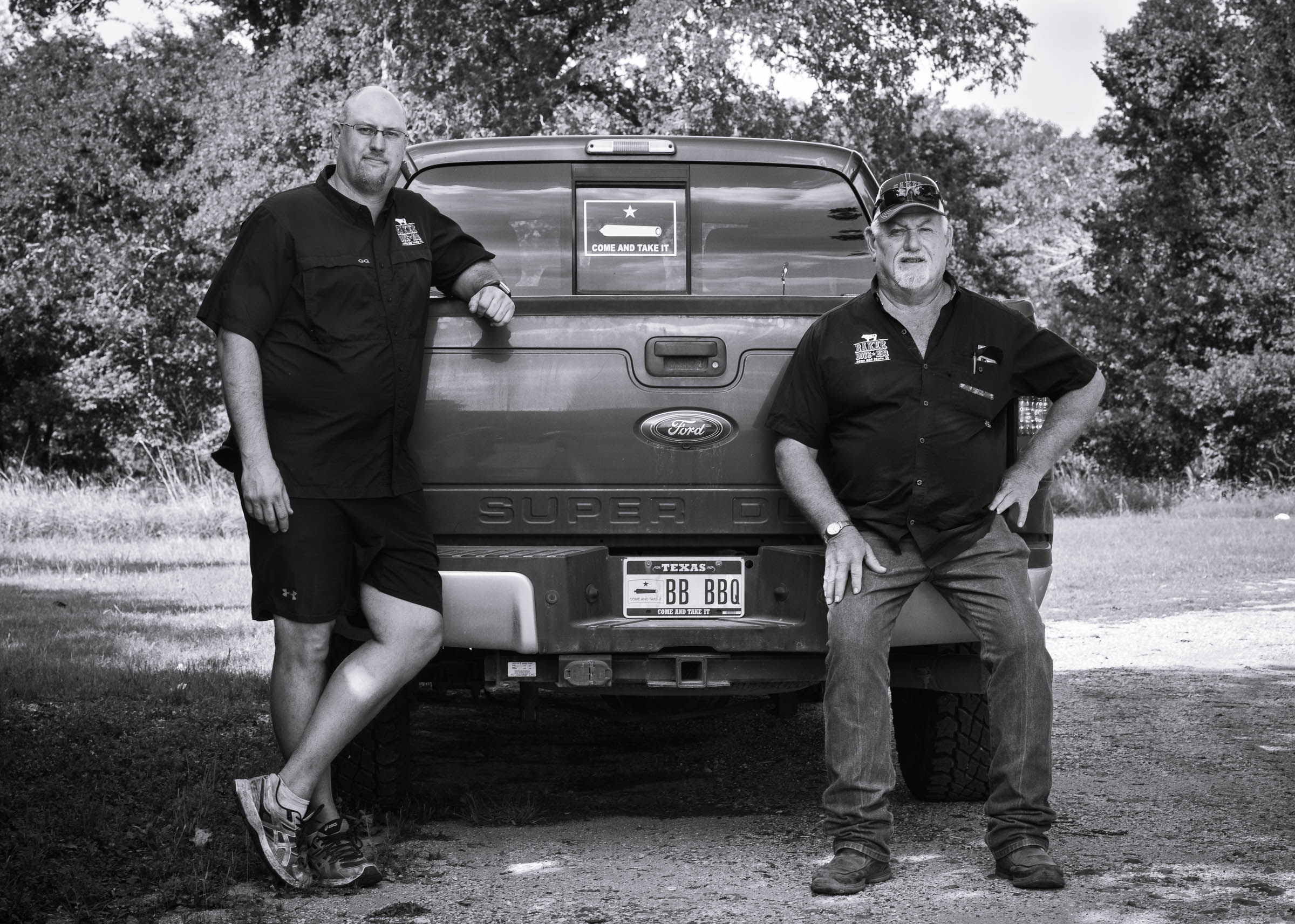 Black-and-white portrait of the owners of Baker-Boys-BBQ, seated on their pick-up truck.