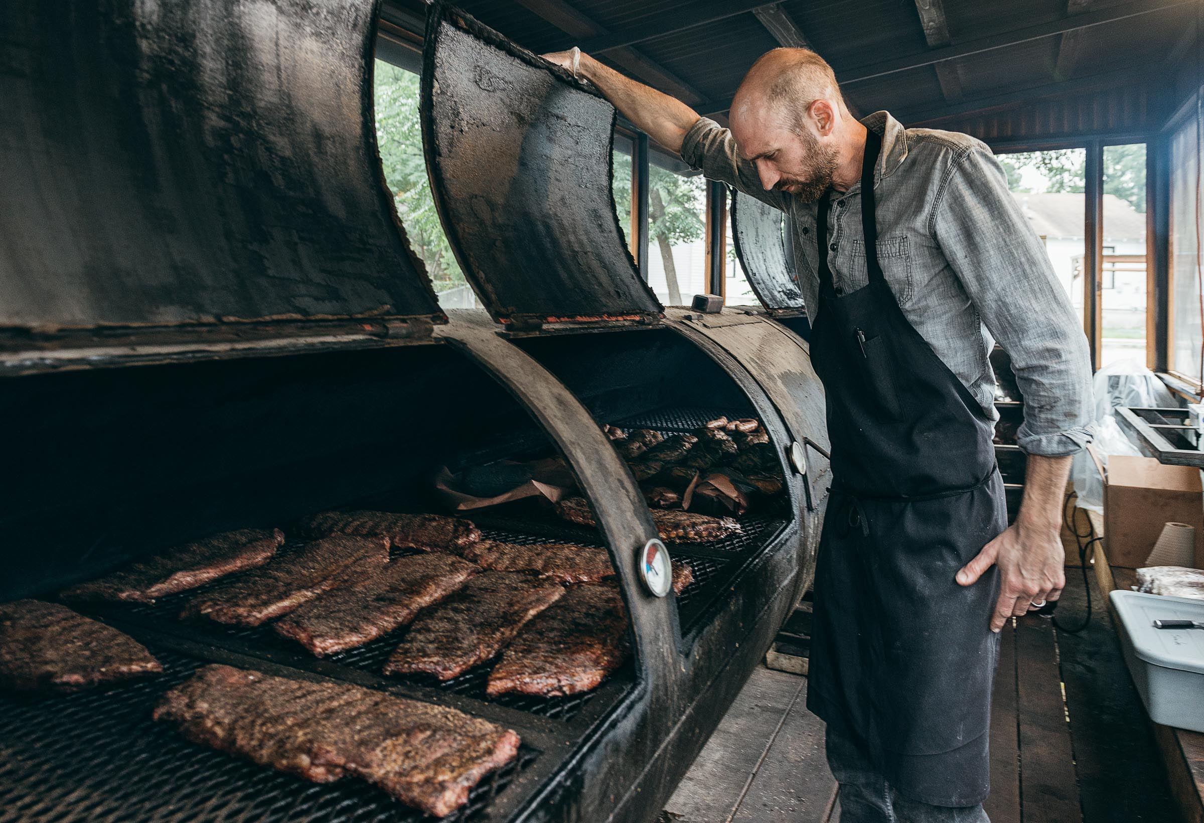 A tall, aproned man tending the meat smoker at Mickelthwaite-BBQ-Austin-TX