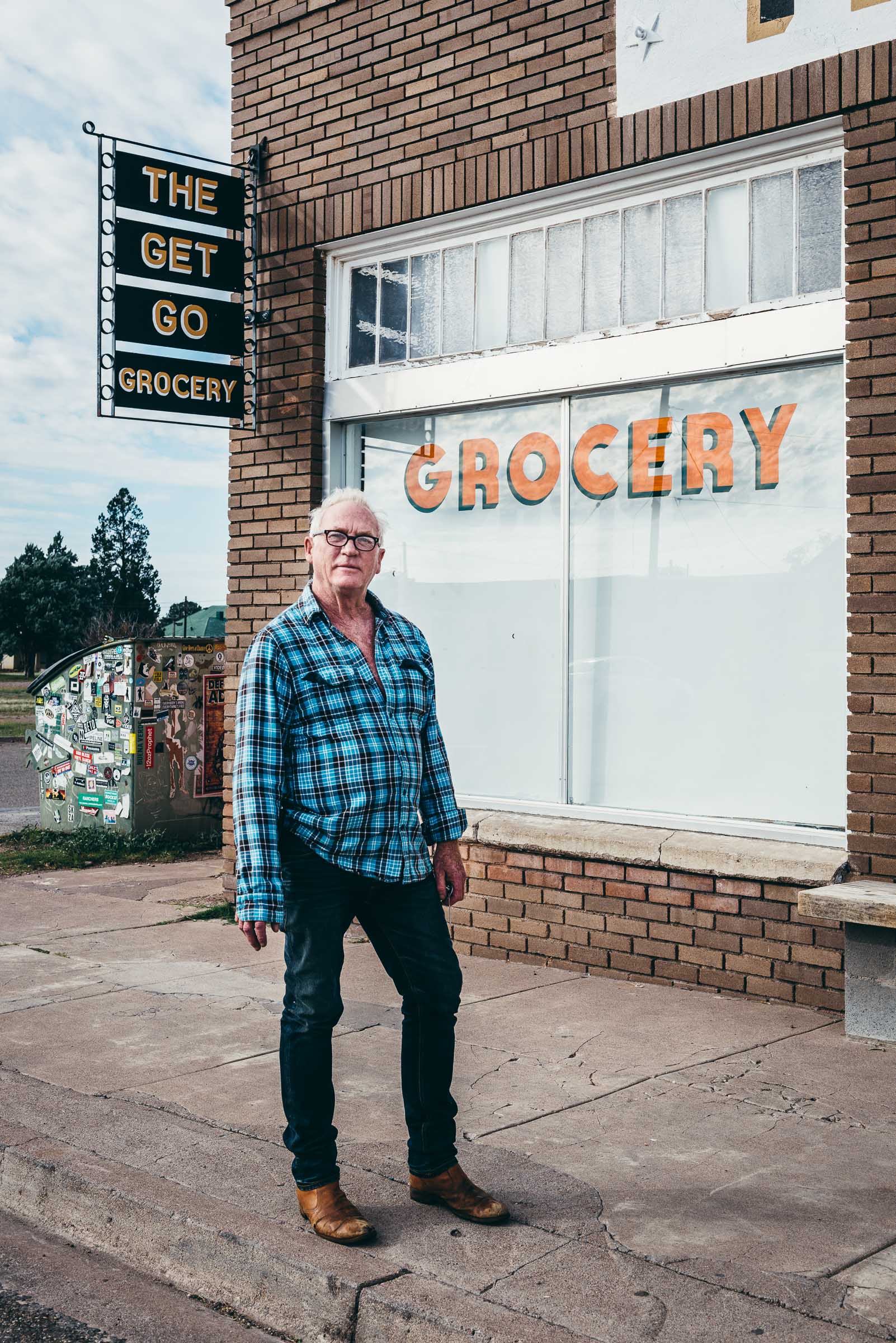 Travel portrait, a lone man in plaid shirt outside The Get Go Grocery in -Marfa-TX.