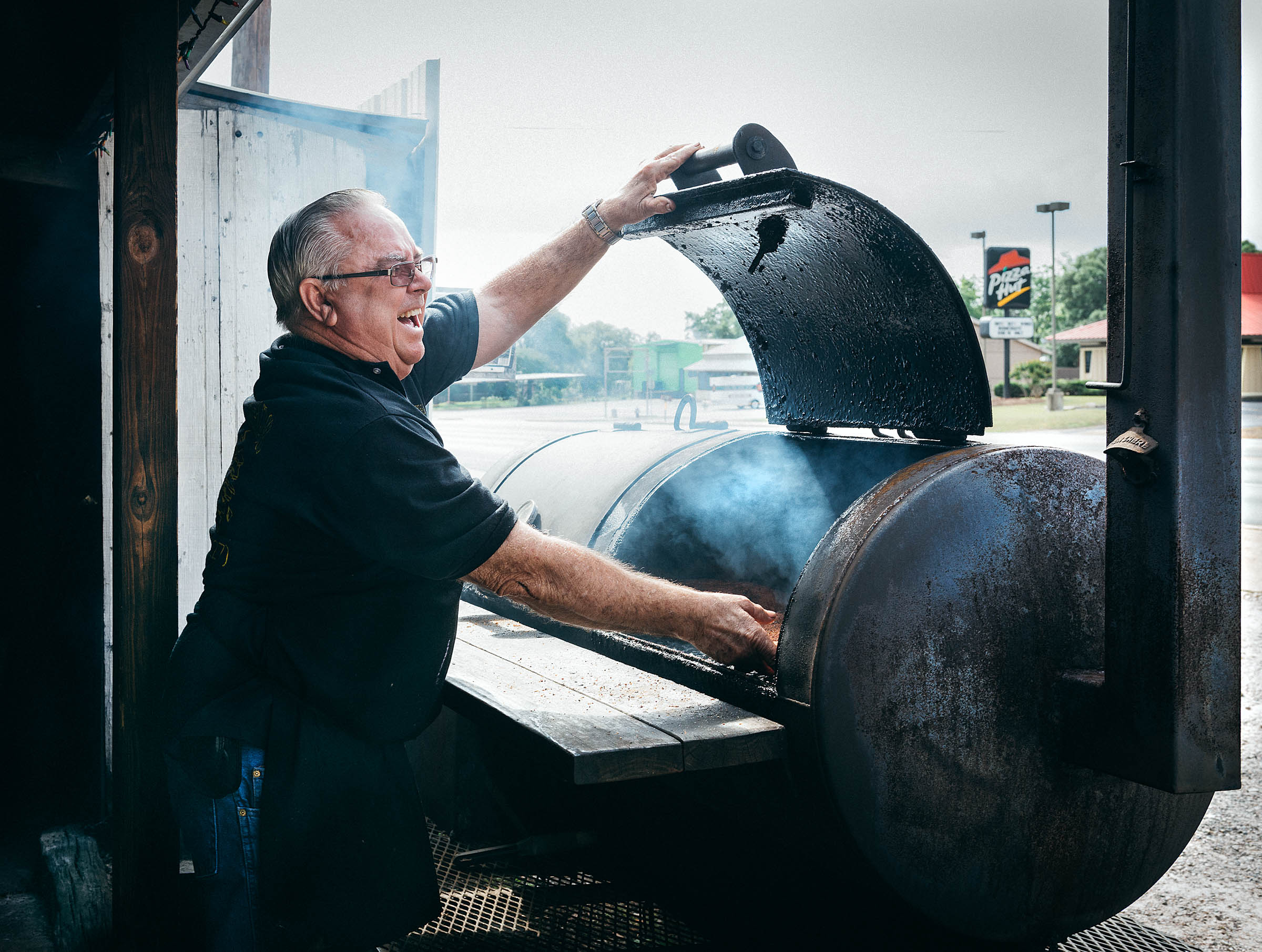Pit-master Robert Payne of Paynes-BBQ in Burnet TX laughing as he opens his meat smoker.